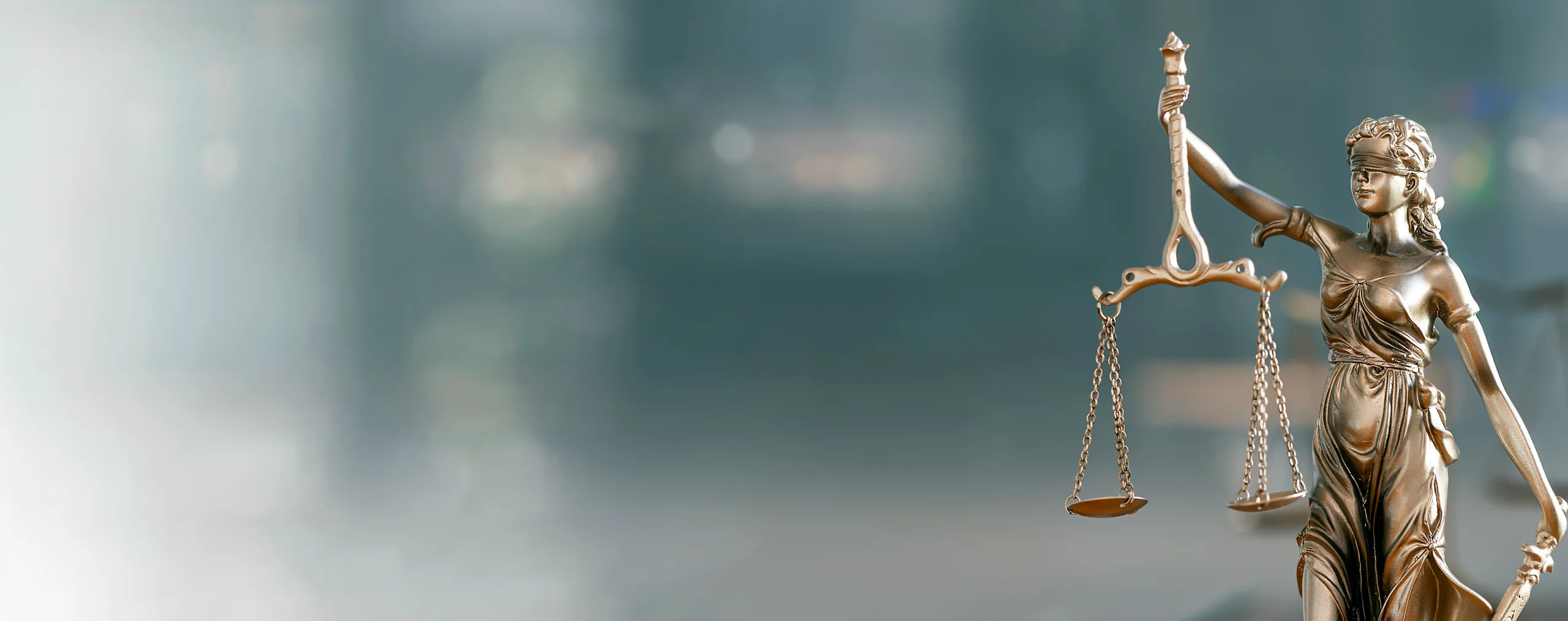 A bronze statue of the blindfolded Lady Justice holding the scales of justice against a blurred teal background.